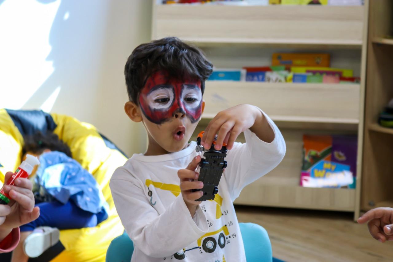Child with face paint playing with a toy vehicle in an educational and playful environment at IVY STEM International School.