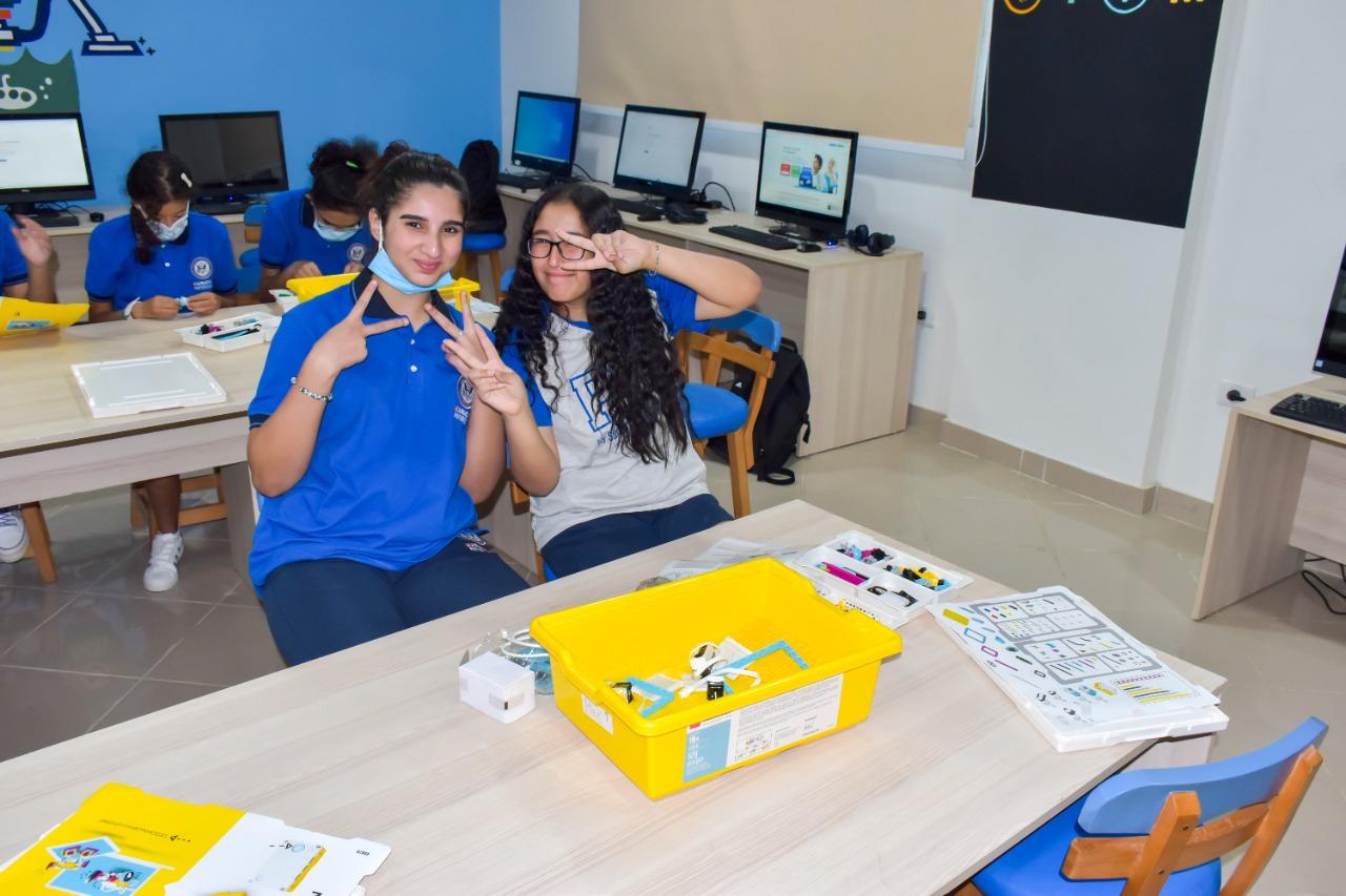 A group of students in a classroom at IVY STEM International School, wearing uniforms and smiling while engaging in educational activities. The classroom is equipped with computers and educational materials, creating a modern and engaging learning environment.