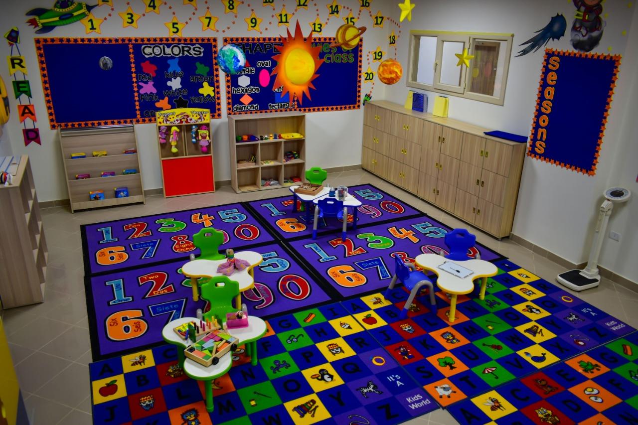 Colorful classroom designed for young children at IVY STEM International School. The room features educational rugs, learning materials, decorations, storage units, wall mirrors, educational boards, ceiling decor, and an air conditioner. It is a stimulating and engaging environment for children to learn and play.