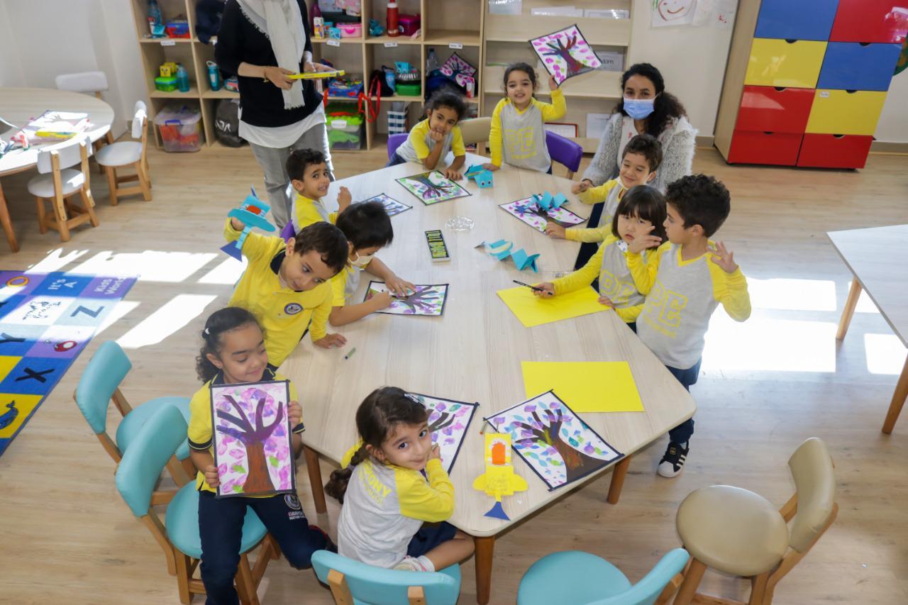 A cheerful classroom scene at IVY STEM International School, where children wearing bright yellow tops engage in art and craft activities. The room is filled with educational toys and resources, promoting a playful and learning-focused environment.