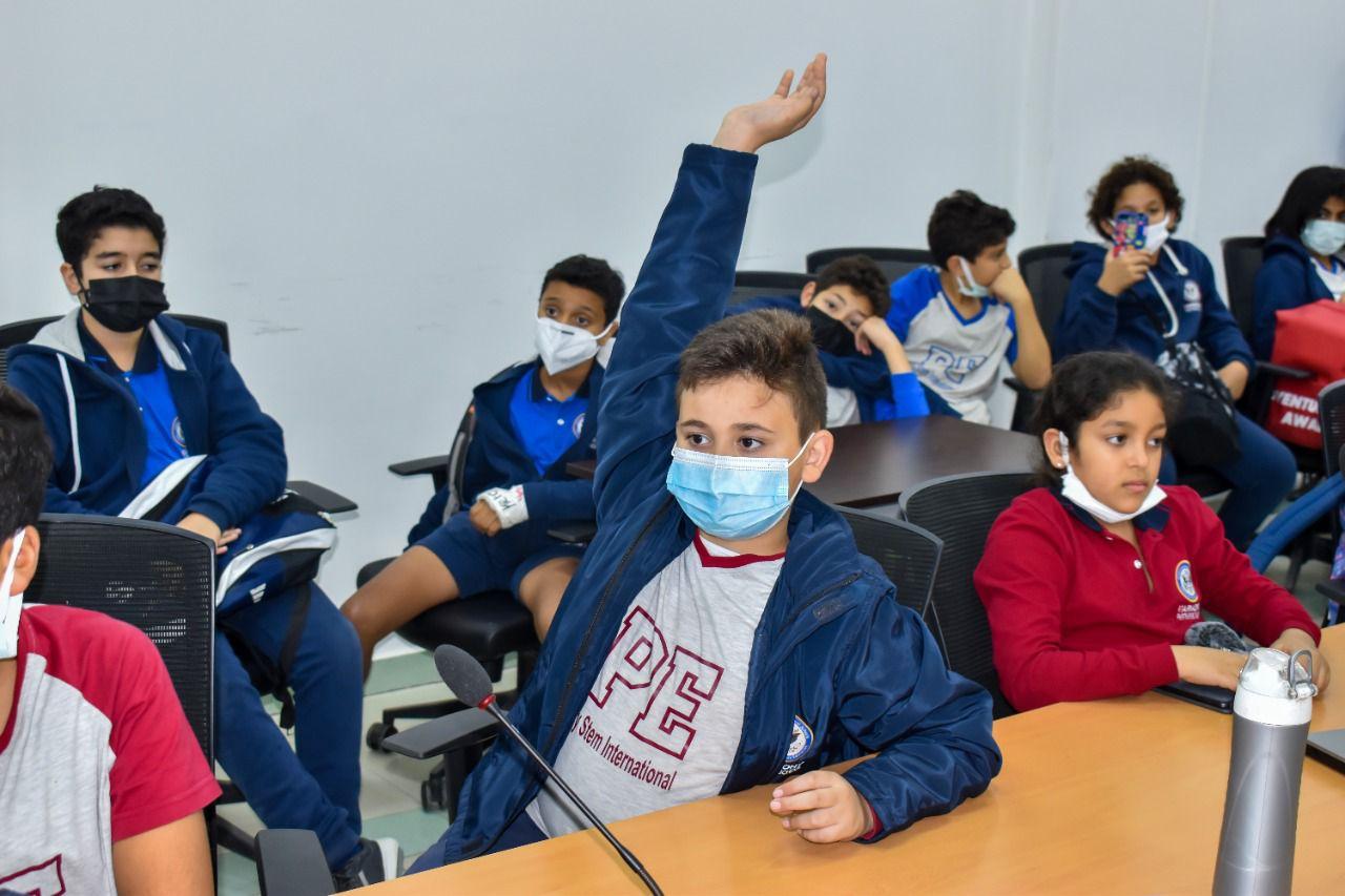 A group of school children at IVY STEM International School engaged in interactive learning in a classroom setting. Students wearing protective face masks participate in a discussion, showcasing the school's commitment to health measures during the COVID-19 pandemic.