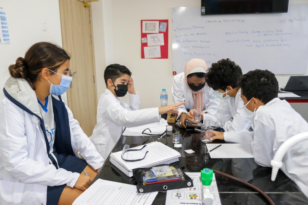 Students at IVY STEM International School conducting a science experiment in a well-equipped laboratory. They are wearing lab coats and face masks, ensuring safety measures. The interactive learning environment promotes hands-on experience with scientific concepts.