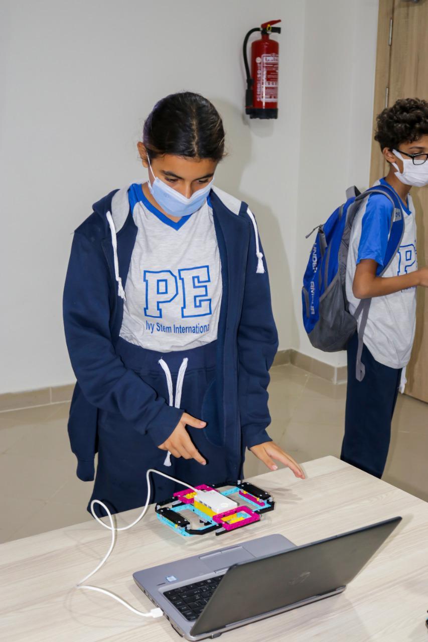 A young student from IVY STEM International School actively participates in a STEM-related educational robotics activity in a classroom, following safety protocols during the COVID-19 pandemic.