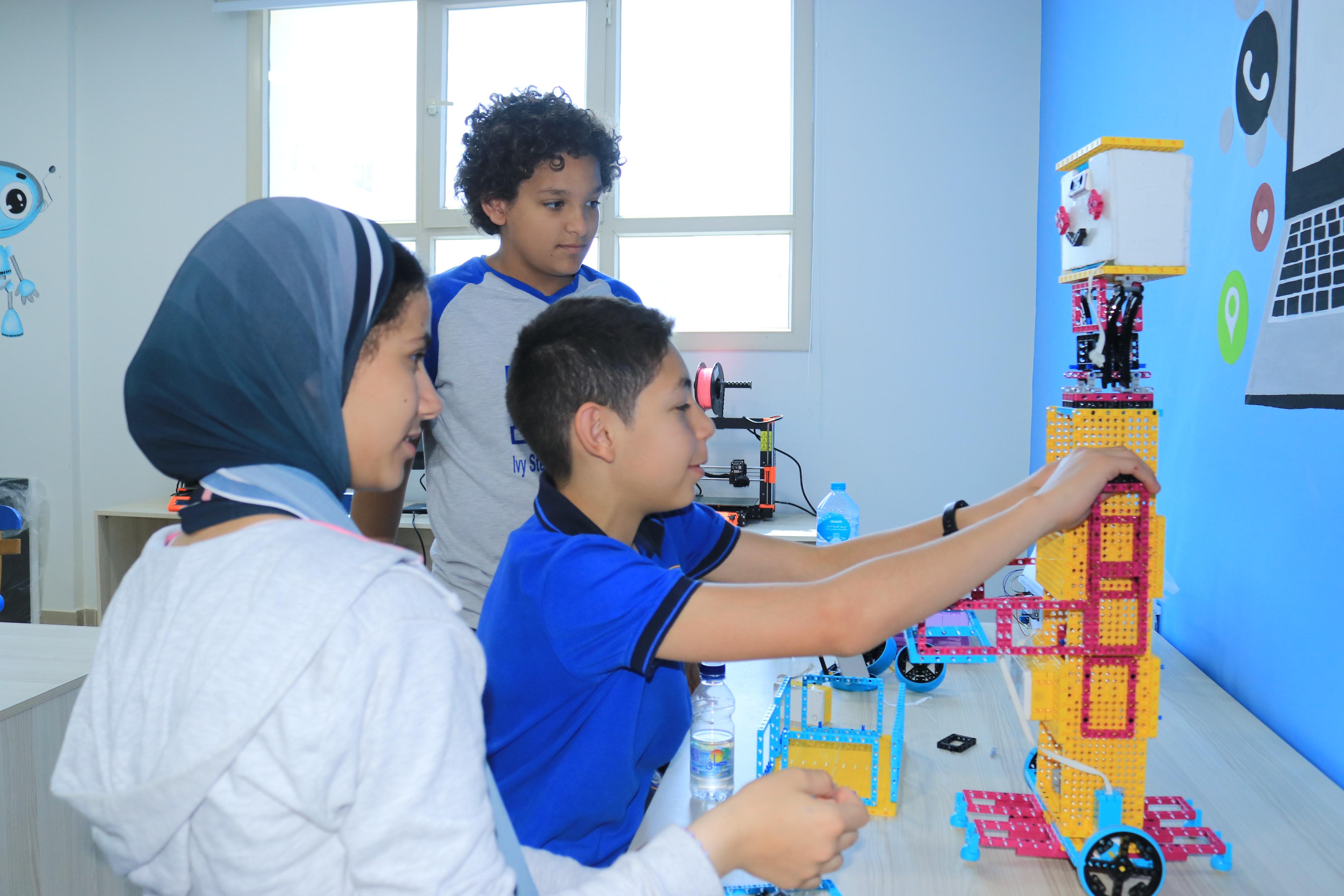 Three young students from IVY STEM International School actively participating in a STEM activity involving a robotic model.