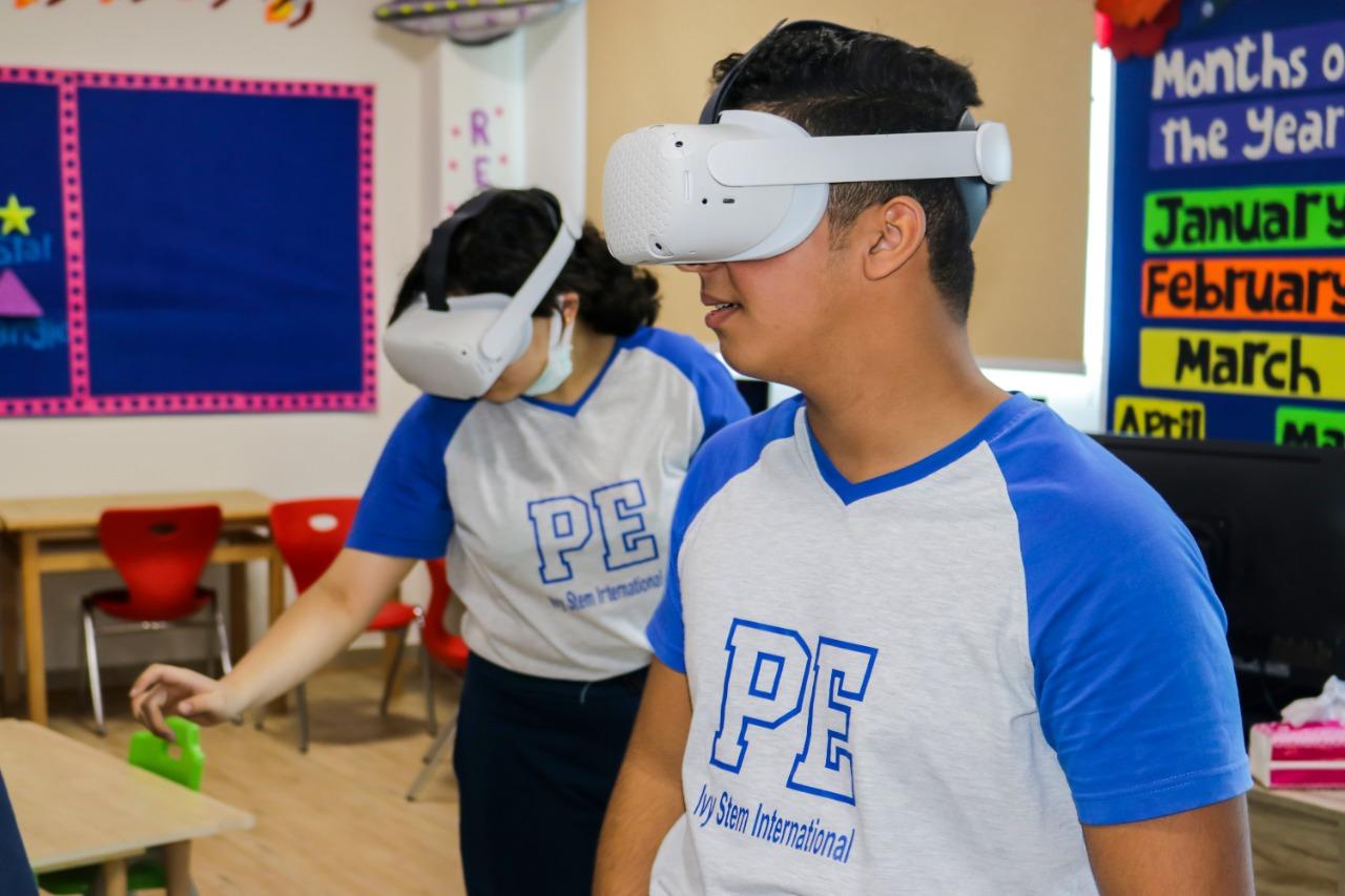 Two individuals wearing VR headsets in a classroom setting at IVY STEM International School. Educational posters about the months of the year can be seen in the background. The individuals are engaged in immersive learning activities using VR technology, showcasing the school's commitment to innovative education.